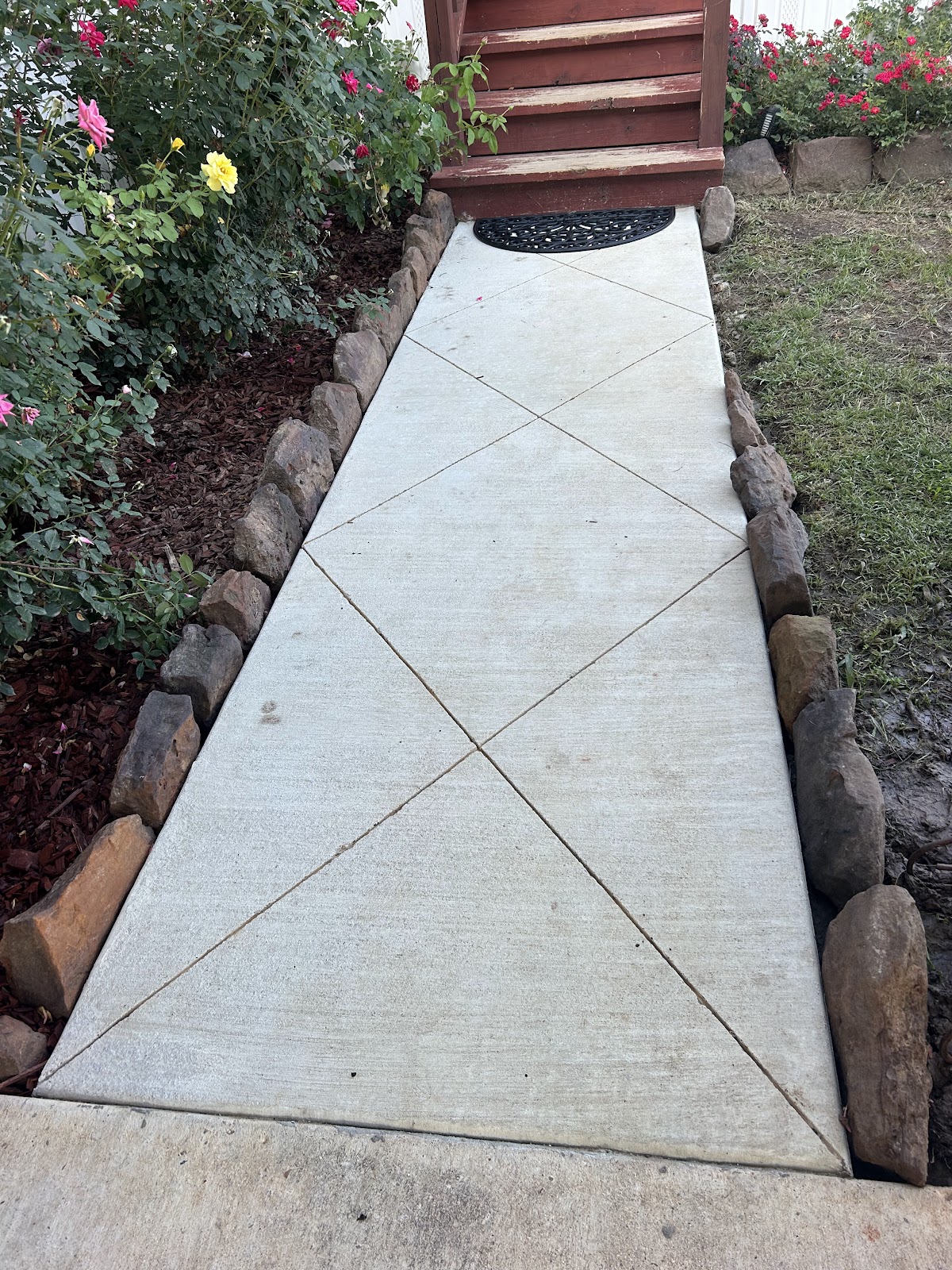 Broom finished walkway with diagonal scoring next to a flower bed